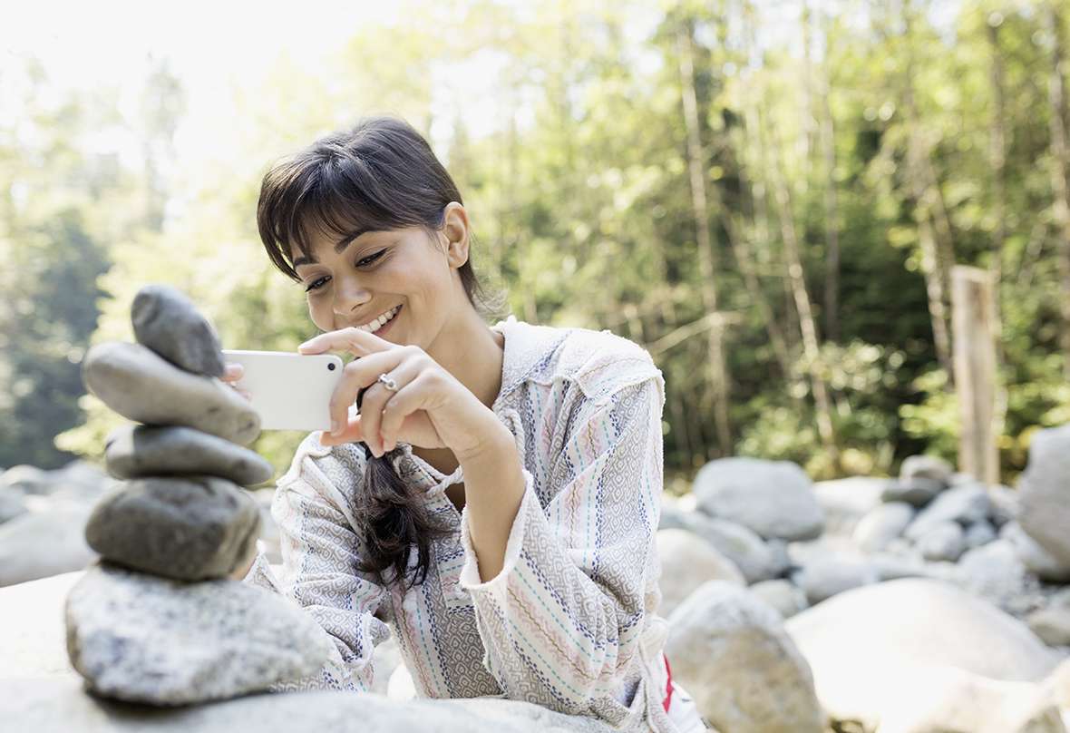 Bild einer lachenden Frau die ein Handy in den Händen hält um ein Foto zu machen.