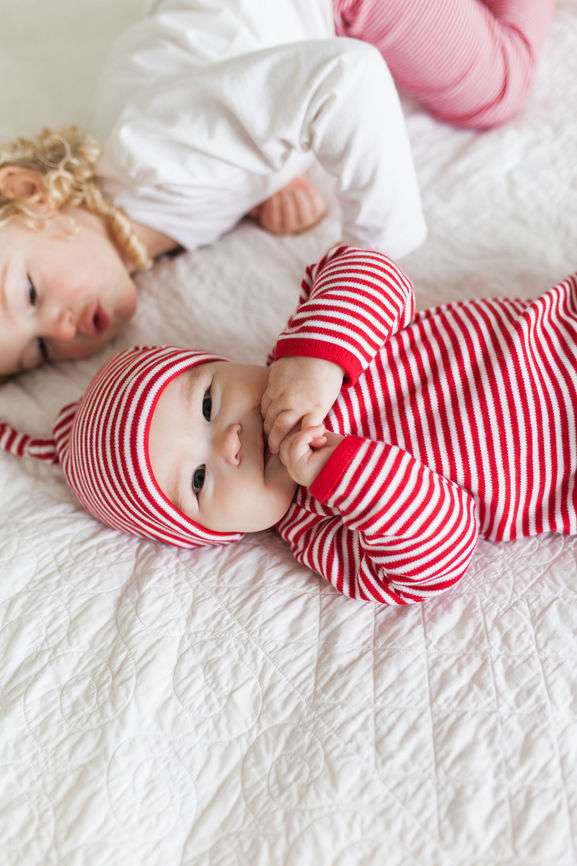 Baby in rot-weiß gestreiftem Body und Mütze, mit Schwester.