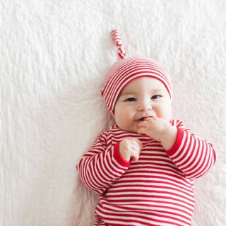 Liegendes Baby in rot-weiß-gestreiftem Body und Mütze knabbert an seiner Hand.