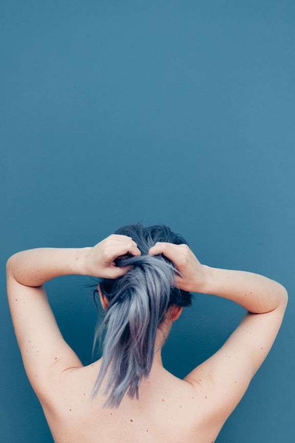 Frau mit grau gefärbtem Haar bindet sich Haargummi in Ponytail