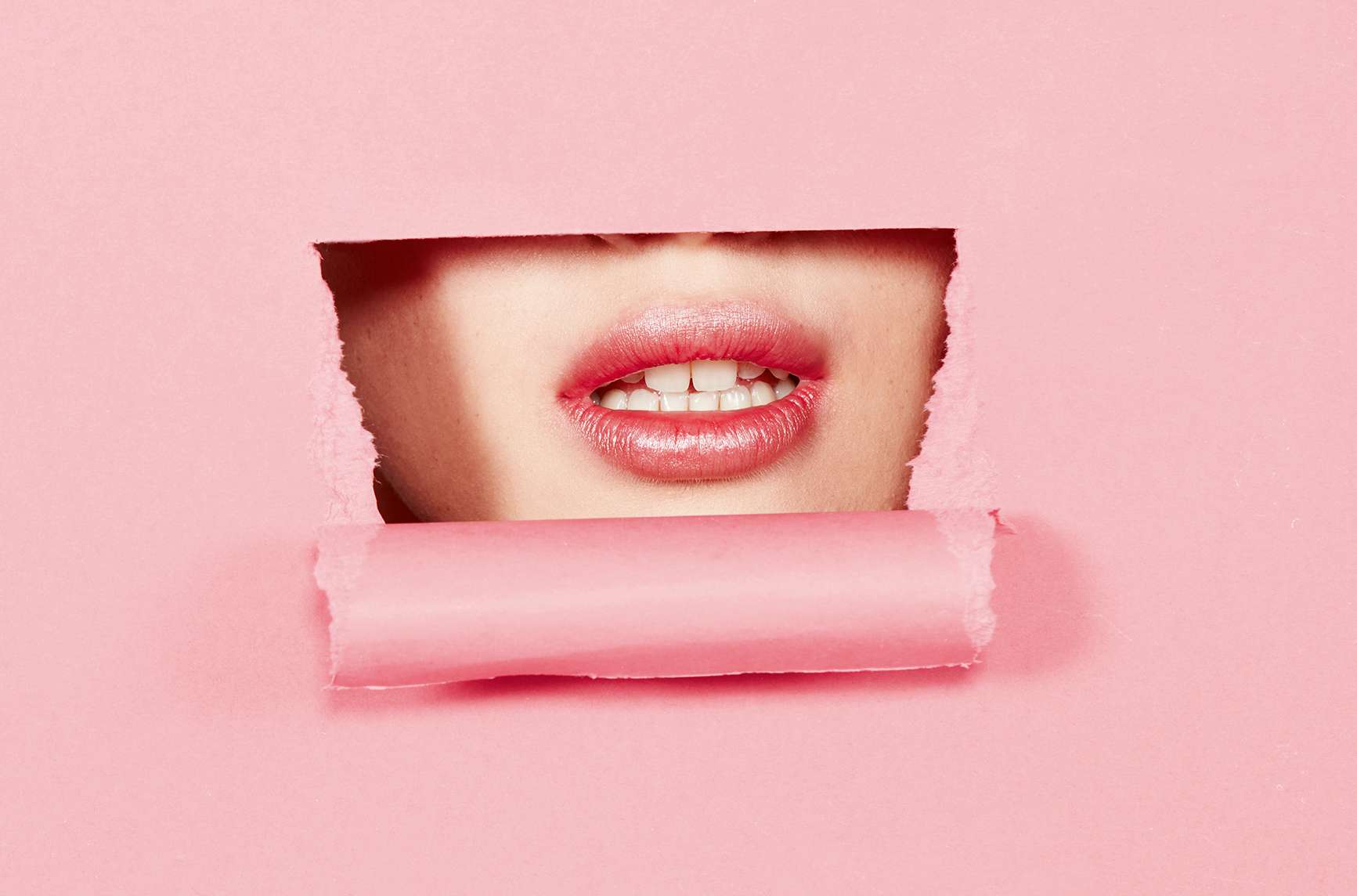 Lippen einer jungen Frau hinter einem rosa Fenster.