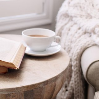Holztisch mit Büchern und Tasse Kaffee, neben gemütlichem Sessel laden ein zum Cocooning