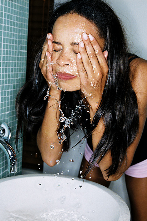 Frau, die sich über einem Waschbecken das Gesicht mit Mizellenwasser wäscht