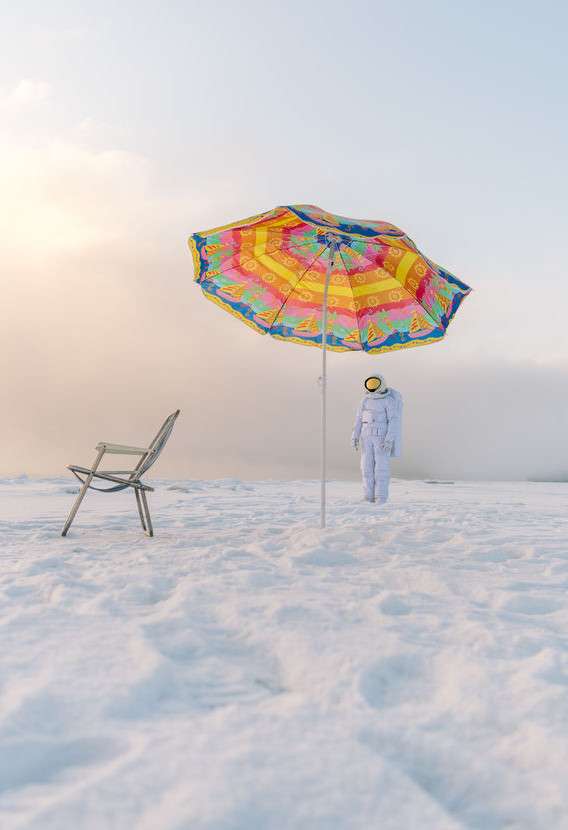 Astronaut im Schnee und ein regenbogenfarbener Sonnenschirm