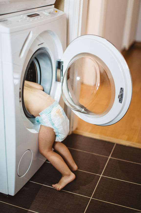 Kind mit Windelpo steckt Kopf in die Waschmaschine