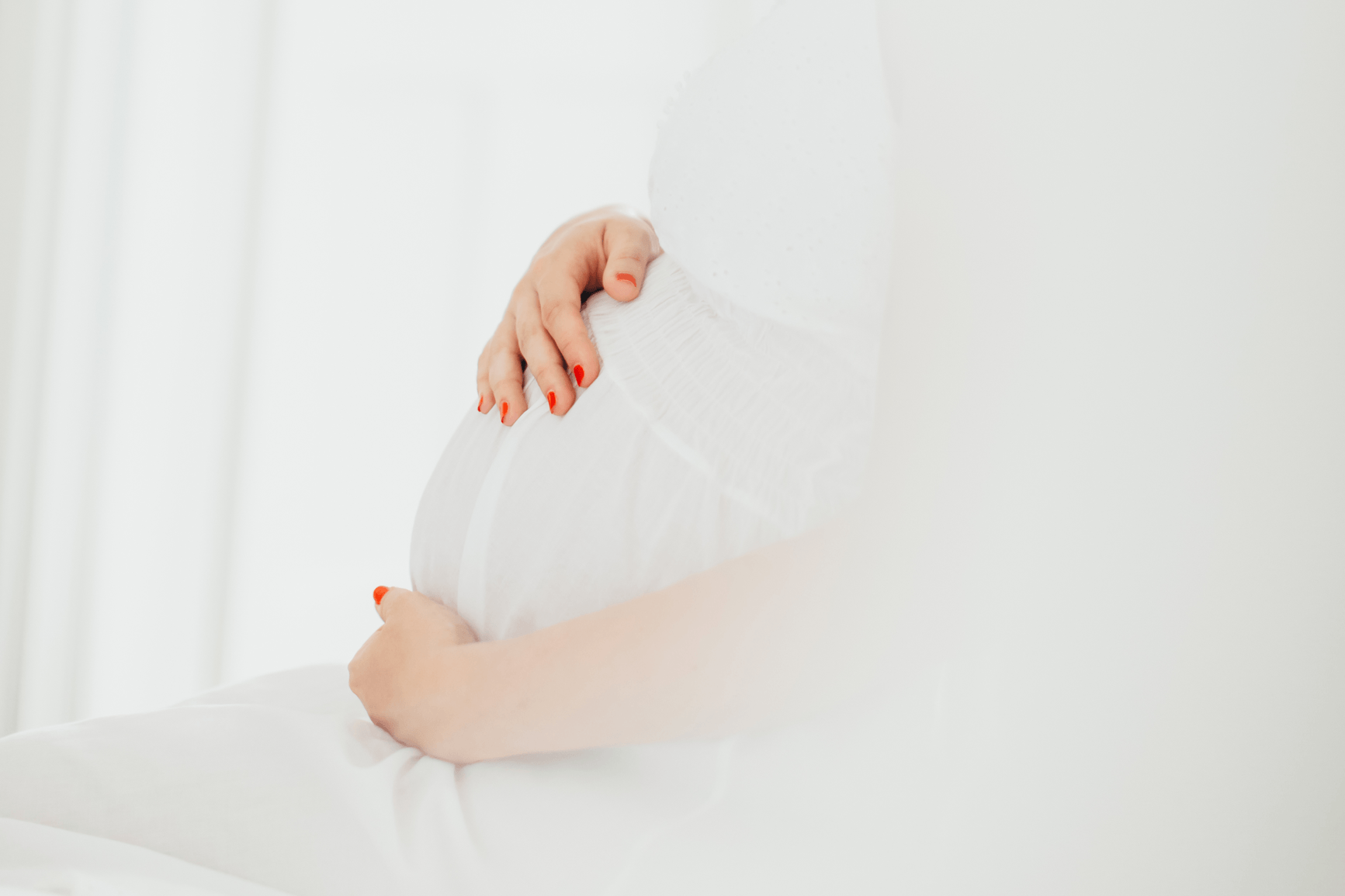 Schwangere Frau in einem weißen Kleid mit roten Fingernägel