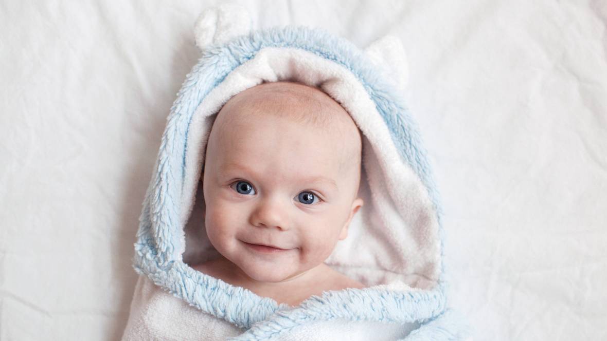 ein Baby in einem Handtuch das fröhlich zu dir hoch blickt