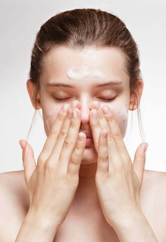Eine junge Frau die ihr Gesicht mit Reinigungsschaum pflegt