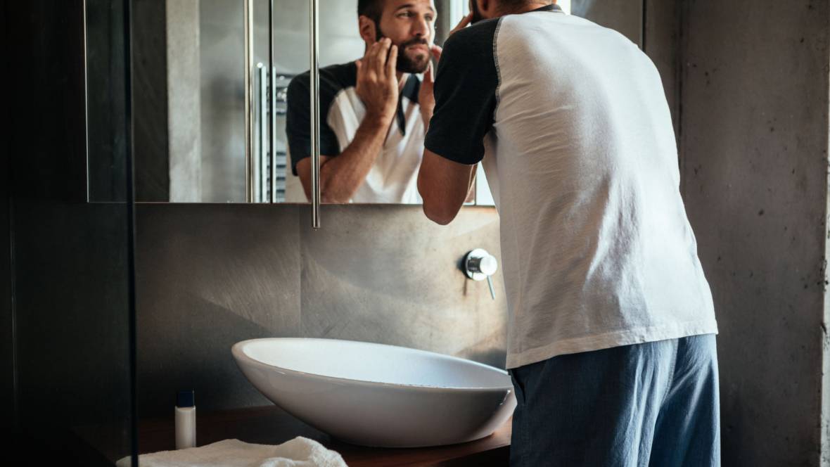 Ein smarter Mann im Jogginganzug der im Badezimmer vor dem Spiegel steht und sich eincremt