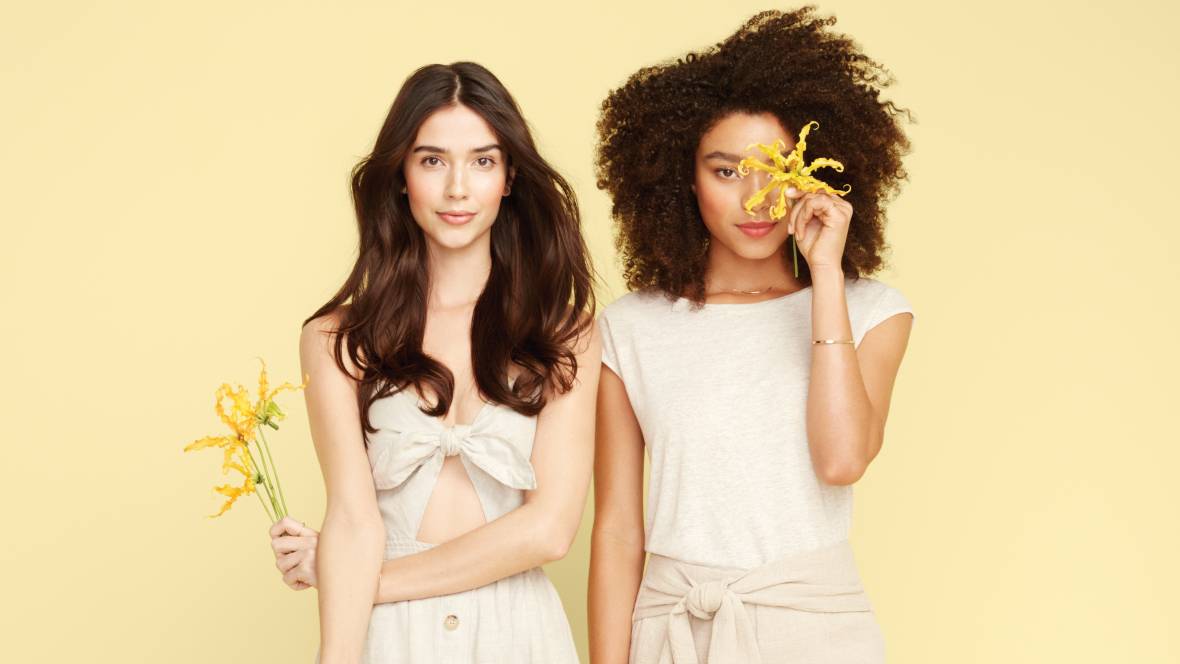 Zwei Frauen vor einem gelben Hintergrund die eine gelbe Blume in den Händen halten
