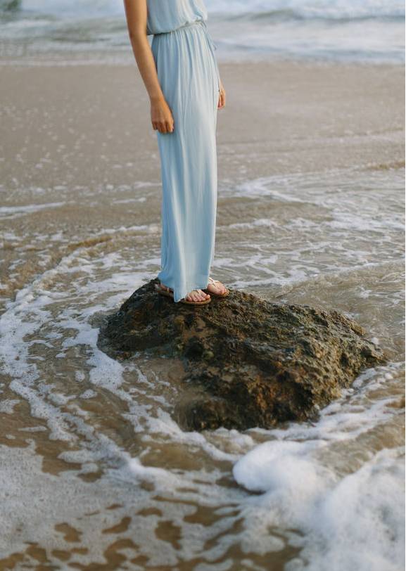 Eine Frau die am Meer auf einem Stein steht und sich ihre schönen gepflegten Füße sonnt