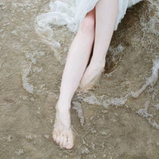 Eine Frau die am Meeresufer ihre gepflegten Füße ins Meer hält