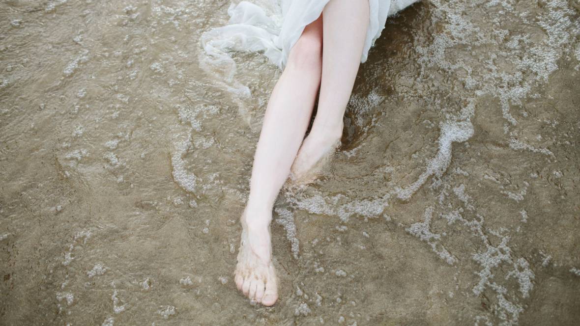 Eine Frau die am Meeresufer ihre gepflegten Füße ins Meer hält