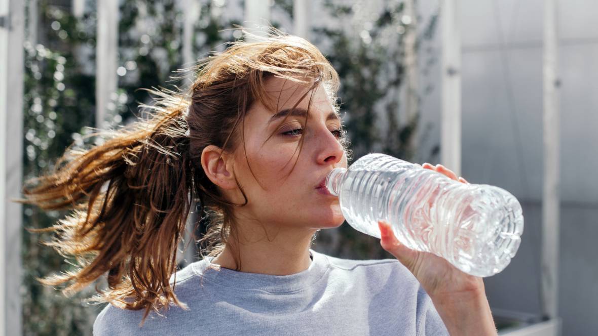 Eine sportliche Frau mit langen braunen Haaren die aus einer Wasserflasche trinkt