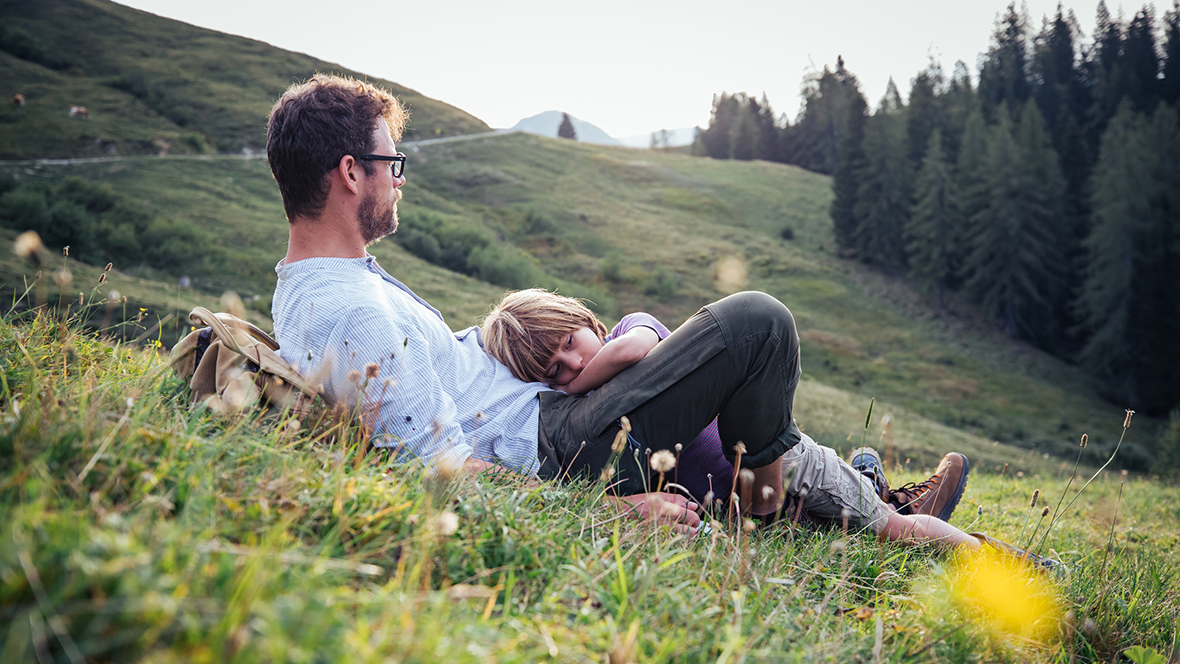 Mann und Kind liegen am Hang im Gras in den Sommerferien 2020 in Österreich zuhause.