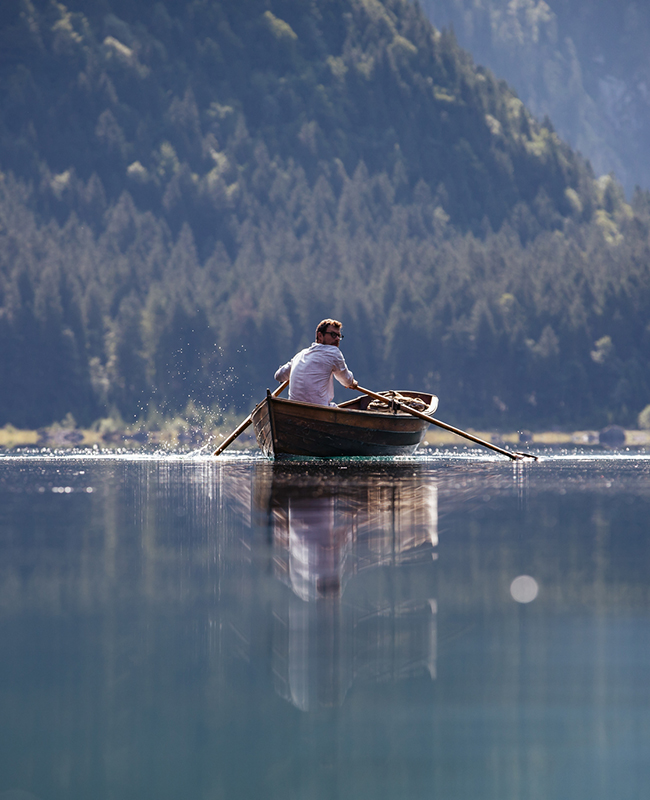 Mann rudert über den See: Eine Idee für Zuhause-Sommerferien 2020 in Österreich.