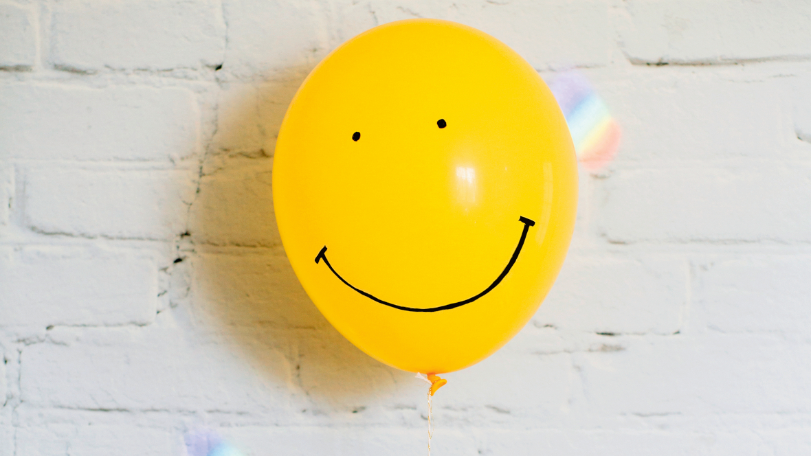 Gelber Ballon mit Smiley-Gesicht vor heller Wand: Lachen macht glücklich und gesund.