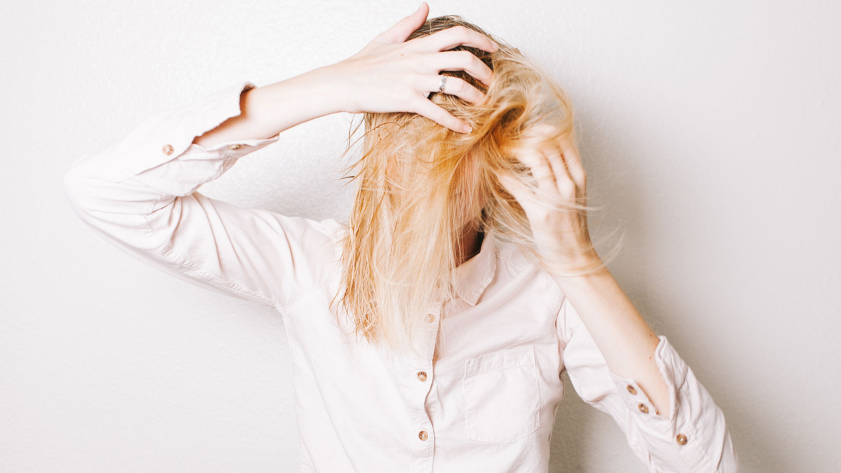 Frau mit blonden Haaren kopfüber und Trockenshampoo im Haar