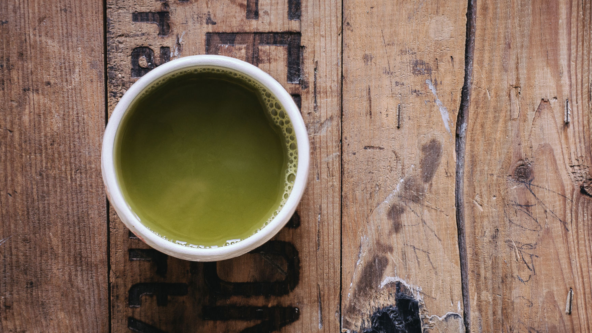 Topshot von Tasse grünem Tee, die auf Holzkiste steht.