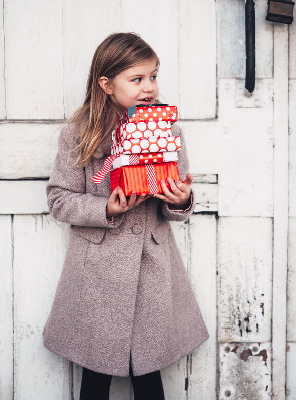 Mädchen in Wollmantel bringt rot eingepackte Weihnachtsgeschenke für Männer