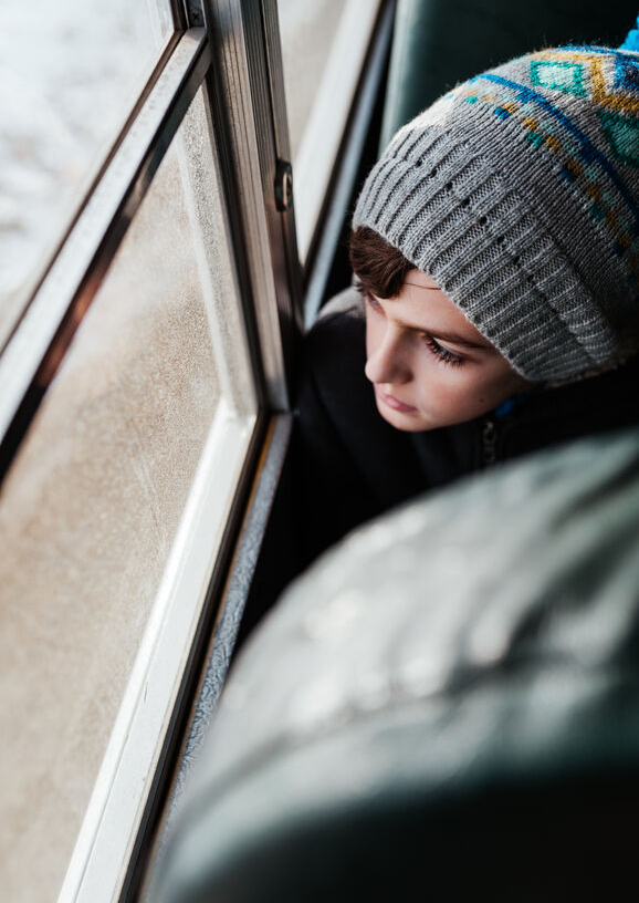 Junge mit grauer Strickmütze blickt aus Busfenster