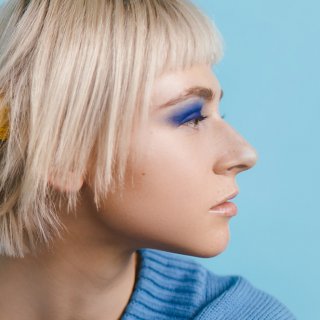 Blonde Frau mit glänzenden Haaren im Seitenprofil und blauem Lidschatten