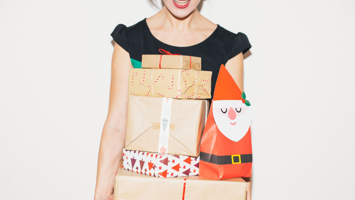 Frau mit vielen Geschenken und Karton-Weihnachtsmann in den Armen