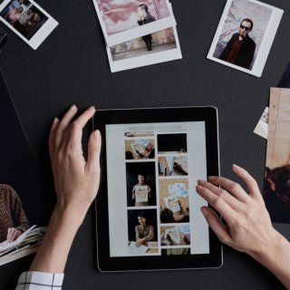 Hände am iPad und ausgedruckte Fotos am Tisch, um ein dm Fotobuch zu erstellen