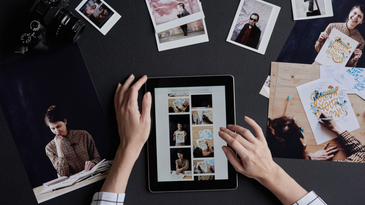Hände am iPad und ausgedruckte Fotos am Tisch, um ein dm Fotobuch zu erstellen