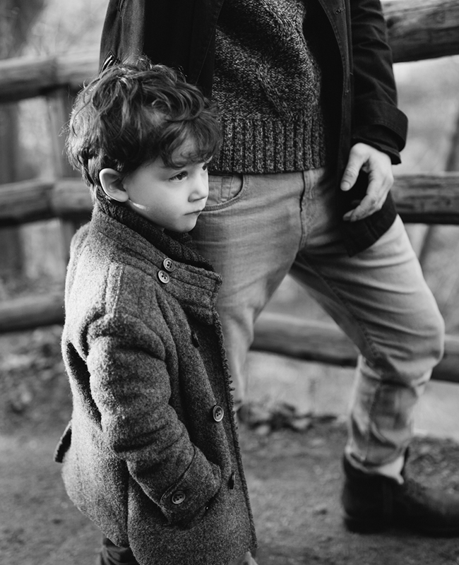 Schwarz-weiß-Foto eines Jungen, der sich an das Bein vom Vater anlehnt