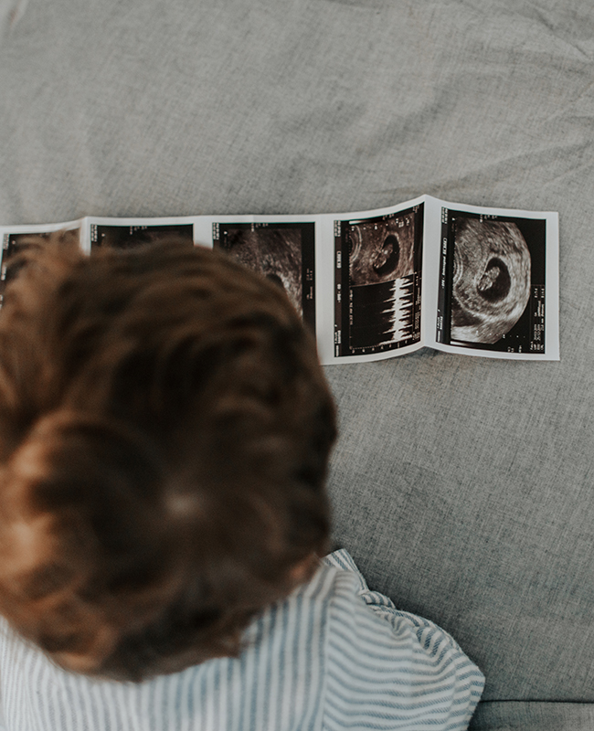 Person beugt sich über Ultraschallbilder eines Ungeborenen.
