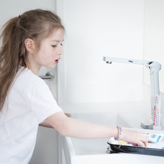 Mädchen im Bad greift zu Zahnseide-Sticks auf dem Waschbecken.