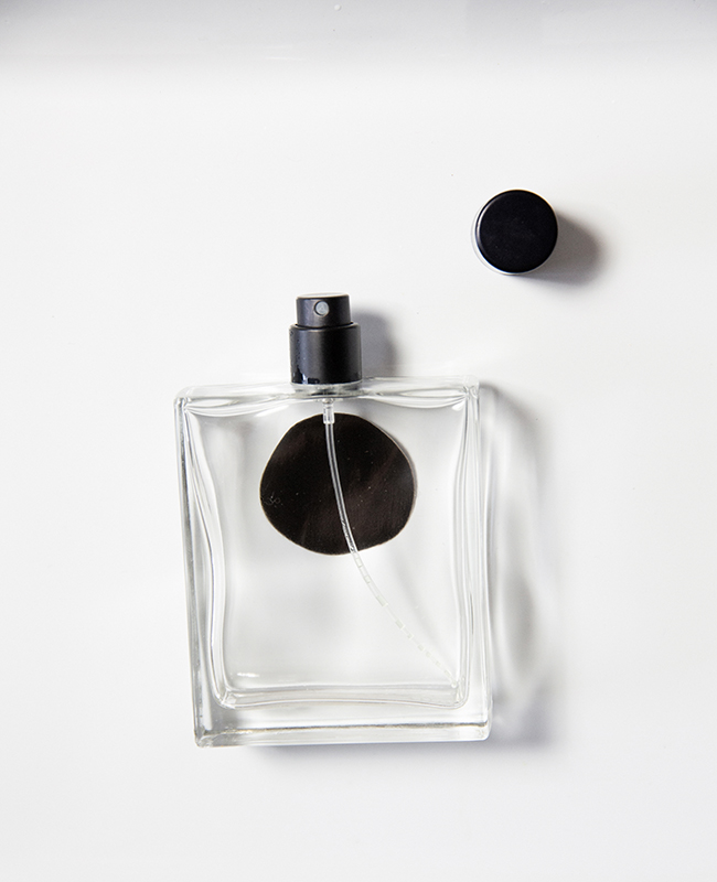 Durchsichtiger Parfumflakon mit schwarzem Punkt und schwarzem Sprühkopf.