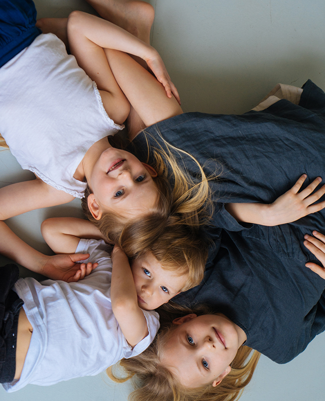 Drei Kinder unterschiedlichen Alters liegen am Boden, von oben fotografiert.