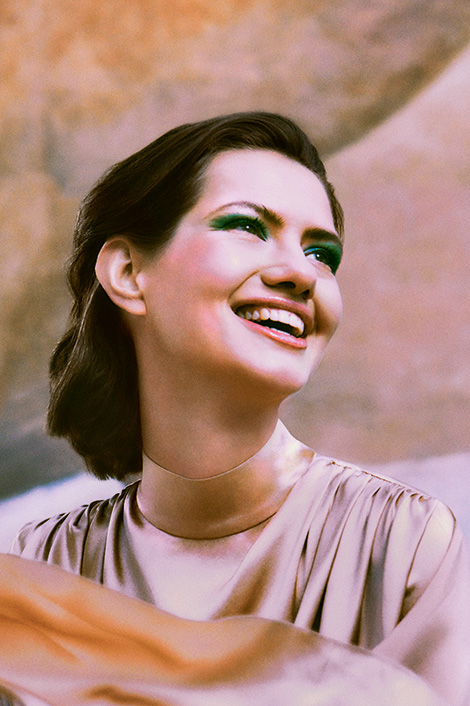 Frau mit breitem Lächeln, grünem Lidschatten und rosa Satinkleid