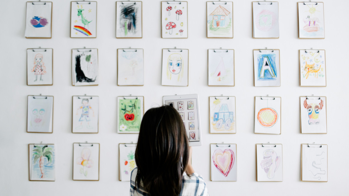 Mädchen steht vor einer Wand mit vielen selbstgemalten Bildern auf Klemmbrettern.