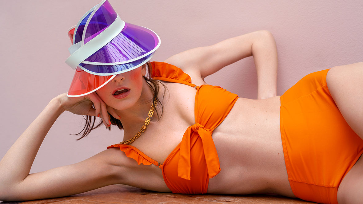 Frau in orangefarbenem Bikini, zum Abkühlen mit drei Schirmmützen halb im Gesicht.