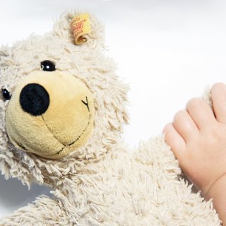 Kinderhand greift nach Arm von Teddybär
