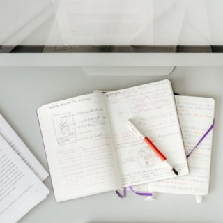 Blick von oben auf einen Schreibtisch voll mit Dokumenten und Notizbüchern