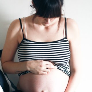 Schwangere Frau, die ihr schwarz-weiß gestreiftes Top über den Bauch hochzieht
