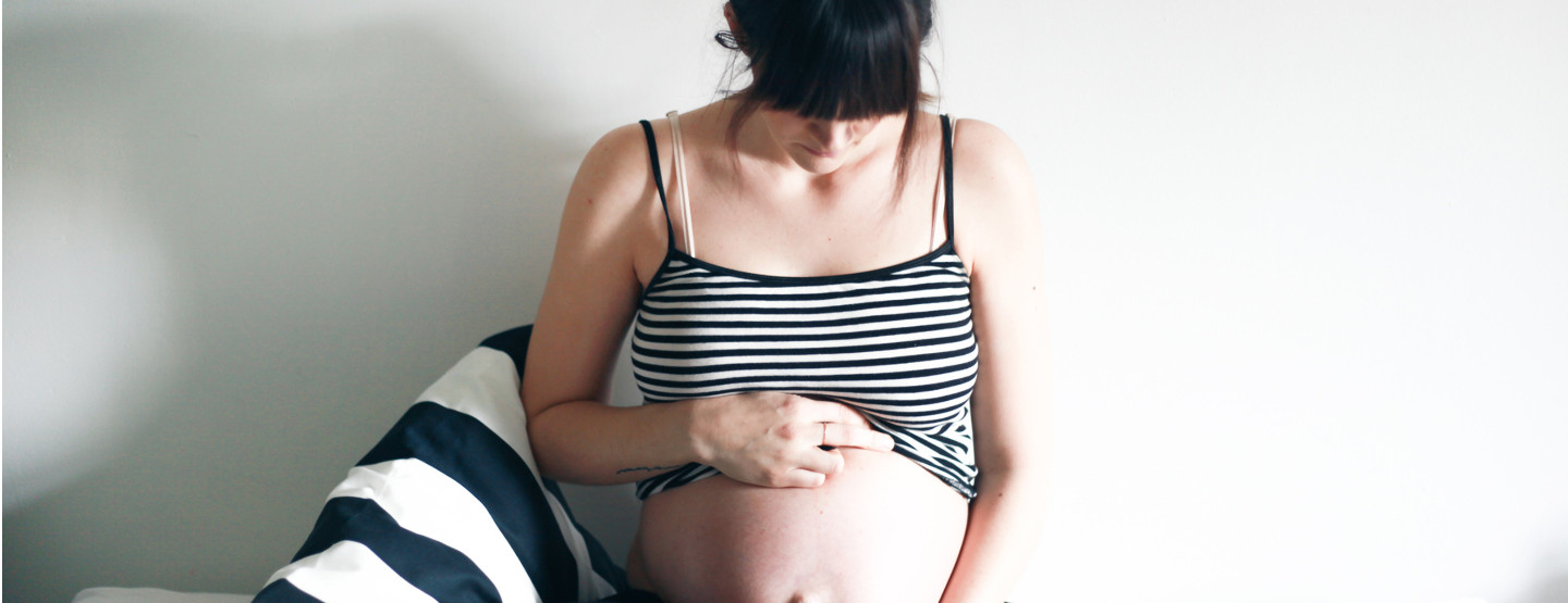 Schwangere Frau, die ihr schwarz-weiß gestreiftes Top über den Bauch hochzieht