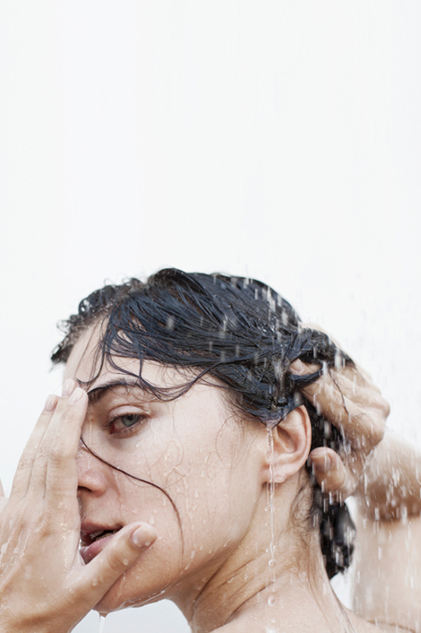 Frau im Regen fährt sich mit den Händen durch die nassen Haare.