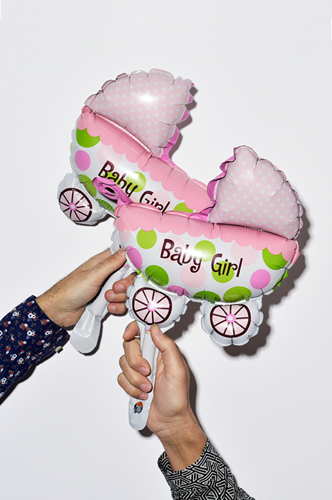 Glückwunsch zur Geburt: Zwei Hände mit Luftballons in Form eines rosa Kinderwagens und dem Aufdruck "Baby Girl"