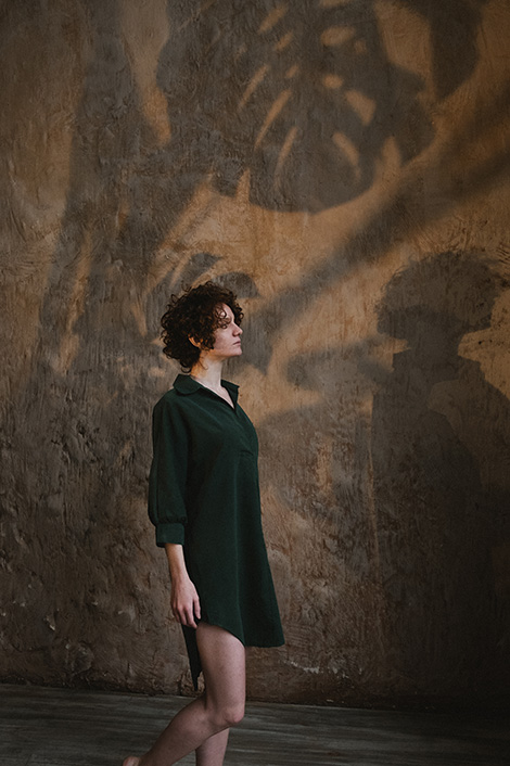 Frau steht neben brauner Wand, auf der sich Schatten von Pflanzen abbilden