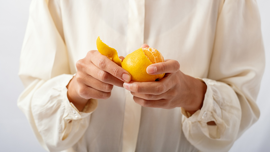Frau, die mit beiden Händen eine Orange schält - vielleicht braucht sie Vitamin C für ihr Immunsystem