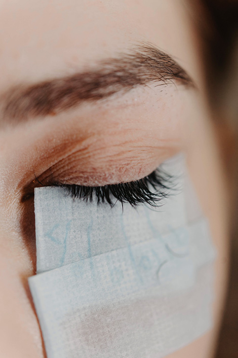 Geschlossenes Auge einer Frau unter deren Auge Pads befestigt wurden, womöglich für eine Wimpernverlängerung