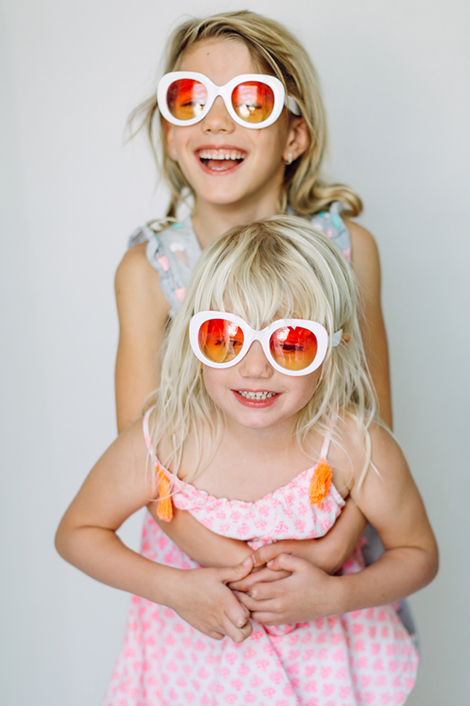 Zwei Geschwister mit bunten Sonnenbrillen umarmen sich.