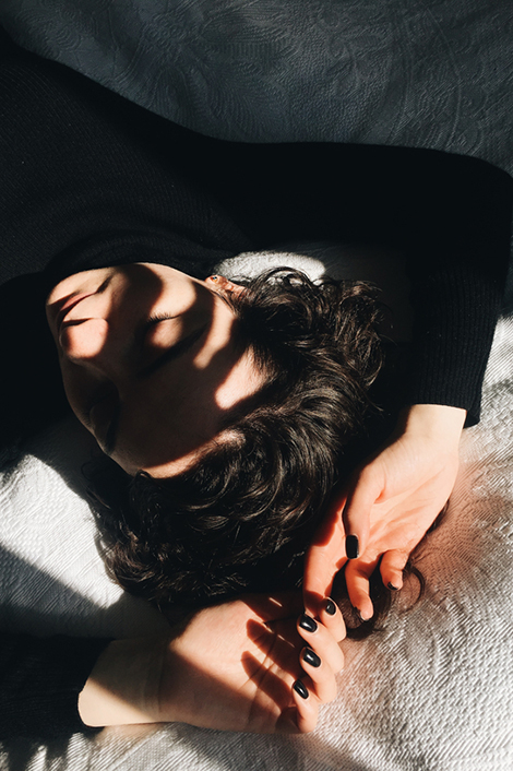 Frau liegt am Bett mit geschlossenen Augen und Schatten im Gesicht - sie leidet unter dem Herbstblues