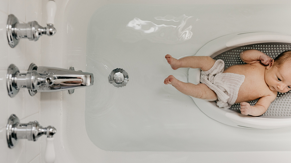 Neugeborenes liegt in Badeschalde in der mit Wasser gefüllten Badewanne