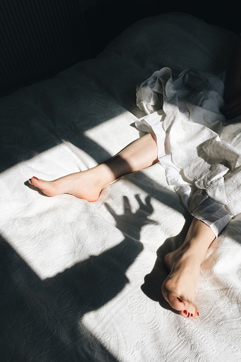Füße einer Frau auf einem Bett - eine Schattenhand, die eine Winterdepression symbolisiert, greift nach ihr